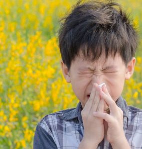 young boy blowing his nose in front of a background of flowers