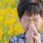 Child blowing his nose against a background of flowers